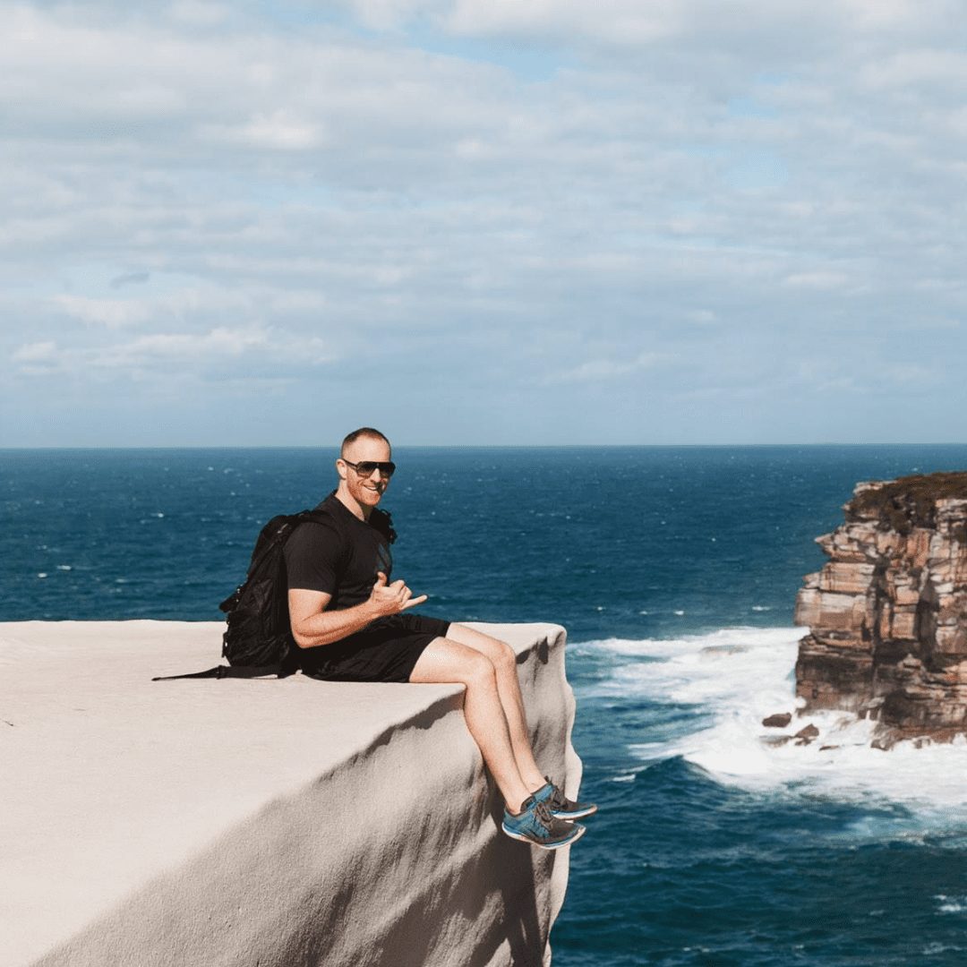 Picture of personal trainer and online coach Rhys Brooks sitting down on a cliff. World class personal training and online personal training, Sydney, Australia